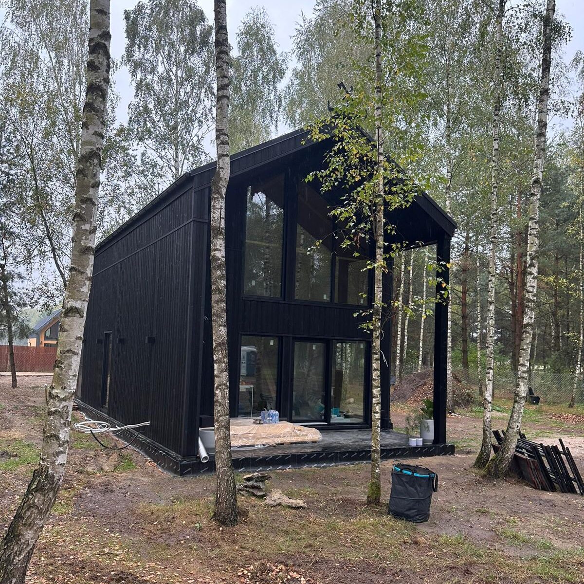 Nowoczesna stodoła Bolimów 2, całoroczny dom modułowy z ciemną elewacją z certyfikowanego drewna w otoczeniu lasu.